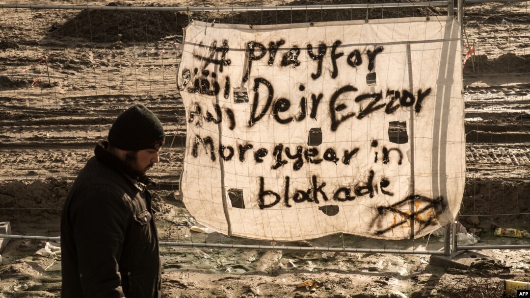 FILE - A man walks past a banner reading "Pray for Deir ez-Zor" at a migrant camp in Calais, France, Dec. 7, 2015. Years of conflict between Syrian government forces and Syrian opposition groups, and the emergence of extremist groups like Islamic State, have forced hundreds of thousands of people to flee from Deir ez-Zor province. 