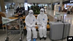 身穿防护服的韩国忠南国立大学工作人员在仁川国际机场等候，为中国留学生提供特别交通服务。（2020年2月25日）