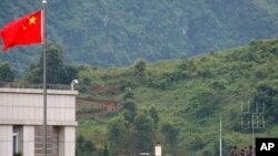 FILE - Pasukan pemerintah Myanmar berdiri di atas atap di sisi Myanmar, dekat bendera China dari kota perbatasan China Nansan di provinsi Yunnan, China barat daya, Minggu, 30 Agustus 2009. (Ng Han Guan/AP)