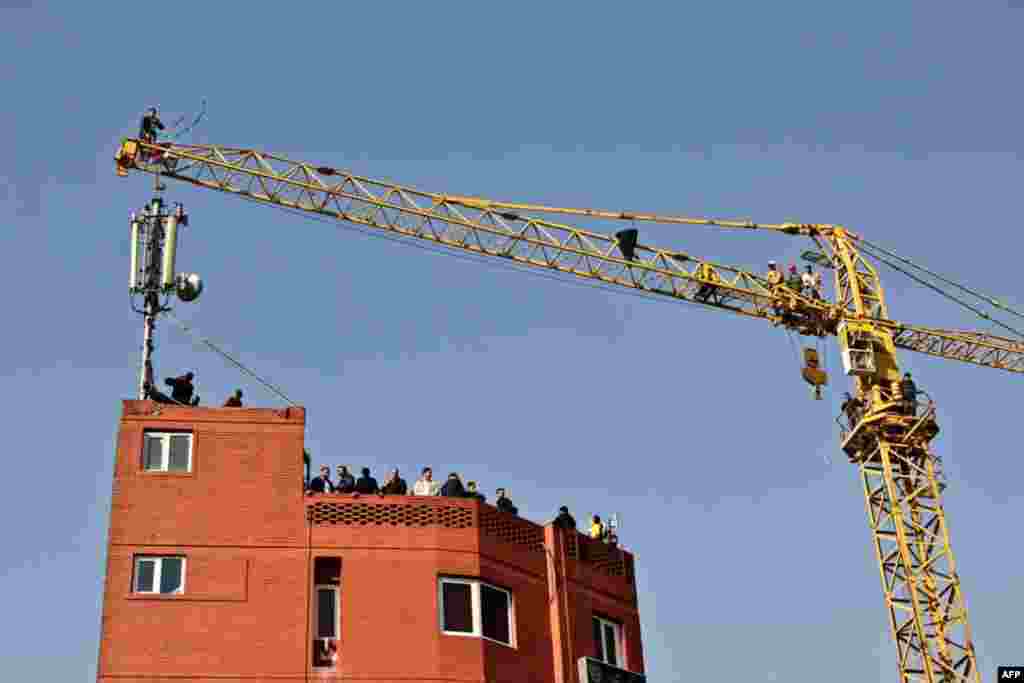 A man wearing a green headband stands on top of a crane before attempting suicide in central Tehran