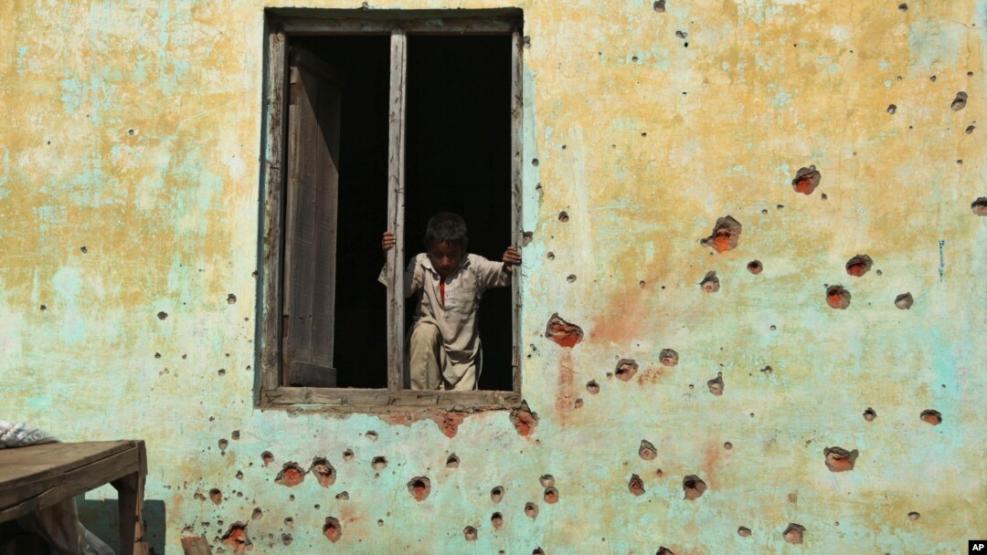 An Indian boy prepares to climb out the window of a house, the walls of which were damaged in mortar shell attack at Jora Farm village, in Ranbir Singh Pura, south of Jammu, India, Feb. 9, 2015. 