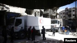 Beberapa orang terlihat di sekitar truk bantuan Bulan Sabit Merah di kota terpencil Douma, Ghouta Timur, Damaskus, Suriah, 9 Maret 2018.