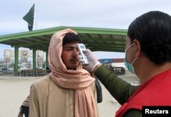 A health worker takes the temperature of a man, who returned from Afghanistan, following the coronavirus outbreak, outside a medical camp near the Friendship Gate, at the Pakistan-Afghanistan border town of Chaman, Pakistan, Feb. 26. 2020.
