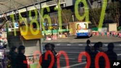 People wait to cross the street in front of an electronic stock indicator in Tokyo, Jan. 21, 2014. 