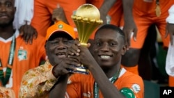 Ivory Coast captain Max-Alain Gradel and President Alassane Ouattara raise Africa Cup of Nations trophy after winning the final against Nigeria, at the Olympic Stadium of Ebimpe in Abidjan, February 11, 2024.