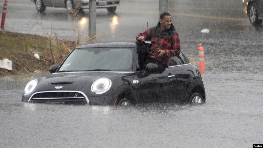 Seorang pengemudi mobil memanjat keluar dari mobilnya yang terjebak banjir di Van Nuys, California, 5 Januari 2016.