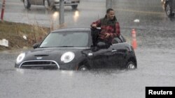 Seorang pengemudi mobil memanjat keluar dari mobilnya yang terjebak banjir di Van Nuys, California, 5 Januari 2016.