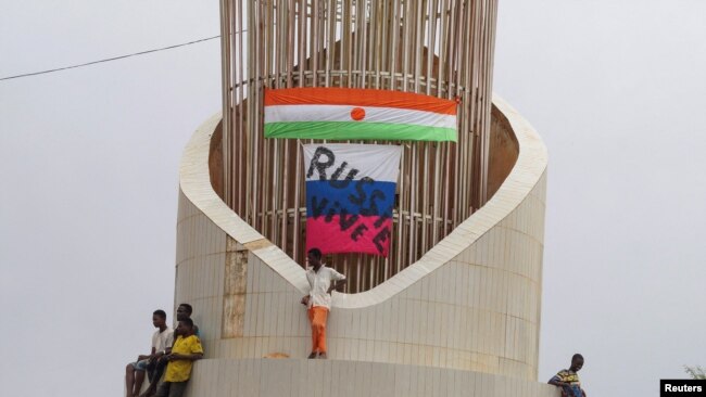 People stand next to Russian and Niger flags while hundreds of supporters of the coup gather in front of the National Assembly in the capital Niamey, Niger July 27, 2023. REUTERS/Balima Boureima