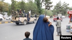 An Afghan woman walks with her children on the anniversary of the fall of Kabul on a street in Kabul