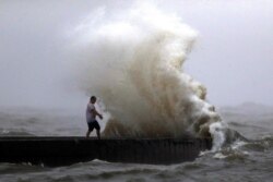 FILE - A wave crashes as a man stands on a jetty near Orleans Harbor in Lake Pontchartrain in New Orleans, June 7, 2020, as Tropical Storm Cristobal approaches the Louisiana Coast.