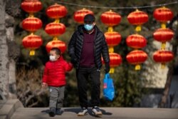 A man and child wearing face masks to protect against the spread of the coronavirus walk past lanterns at a public park in Beijing on Feb. 19, 2021.
