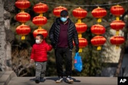 A man and child wearing face masks to protect against the spread of the coronavirus walk past lanterns at a public park in Beijing on Feb. 19, 2021.