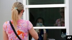 A Parkland Hospital employee behind window, gives verbal instructions to a woman who was self-administering a COVID-19 test at a walk up site in Dallas, June 11, 2020.