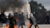 Riot police walk with their gear on fire, after being struck by Molotov cocktails at a protest near the Greek parliament, marking the second anniversary of the country's worst railway disaster, in Athens, Greece, Feb. 28, 2025. 