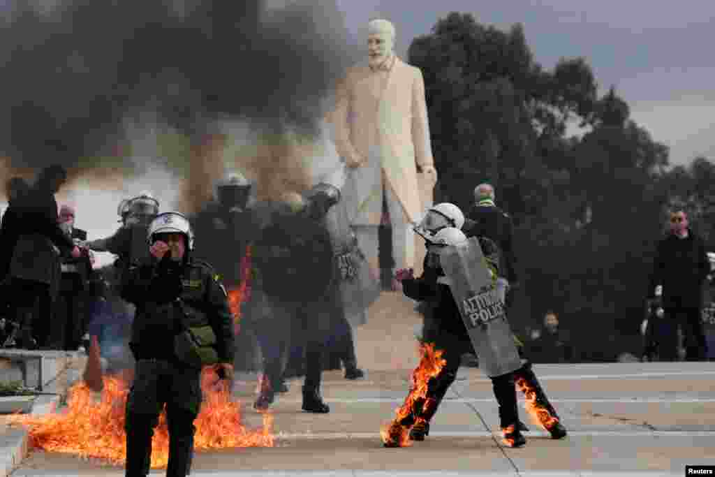 Riot police walk with their gear on fire, after being struck by Molotov cocktails at a protest near the Greek parliament, marking the second anniversary of the country&#39;s worst railway disaster, in Athens, Greece.