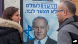 Dos personas conversan frente a un póster del primer ministro de Israel Benjamin Netanyahu, en un centro de votación en Hadera, en el norte de Israel. Diciembre 26 de 2019. Este día se celebraron las elecciones primarias del partido. AP/Ariel Schalit.