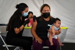 FILE - Laura Sanchez, right, holds her 2-month-old son, Lizandro, while receiving a dose of the Pfizer COVID-19 vaccine at a vaccine clinic set up in the parking lot in Orange, Calif., Aug. 28, 2021.
