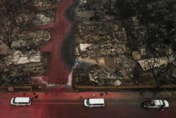 A search and rescue team, surrounded by red fire retardant, is seen near burned residences and vehicles in the aftermath of the Almeda fire in Talent, Oregon, Sept. 13, 2020.