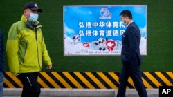 People walk past a poster promoting the 2022 Winter Olympics that reads 'Carry forward the Chinese sports spirit, promote sportsmanship' in Beijing, Dec. 8, 2021.