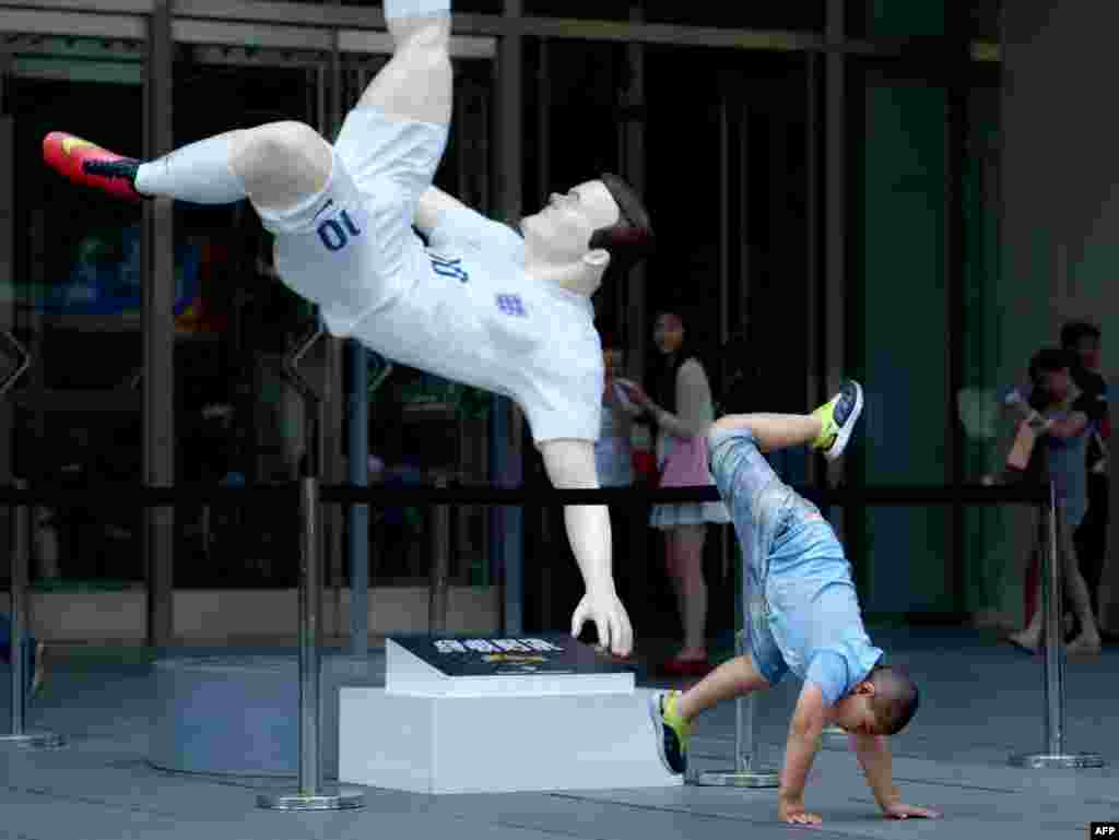 A boy poses for a photo in front of a large figure of England football player Wayne Rooney at the entrance of a mall in Beijing, China.