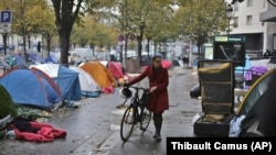 Seorang perempuan berjalan membawa sepedanya melewati tenda-tenda yang dibangun oleh para migran di Paris, Prancis, pada 4 November 2016. (Foto: AP/Thibault Camus)