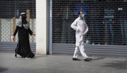 A man wearing a face mask to protect against coronavirus and a woman, walk past shuttered shops on a usually bustling high street as the country continues its lockdown to help curb the spread of the virus, in London, April 27, 2020.