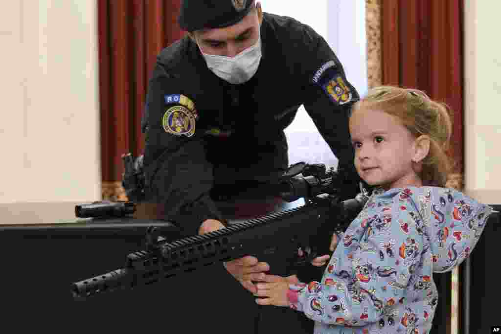 A girl poses with a weapon at a stand set up by Romania&#39;s gendarmerie at the Palace of the Parliament, on International Children&#39;s Day in Bucharest.
