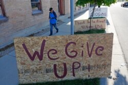 FILE - A man walks past a "we give up" sign outside a shop that closed permanently because of the COVID-19 outbreak, in Salt Lake City, May 8, 2020.