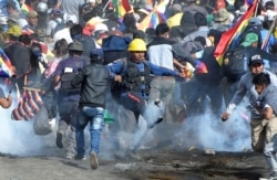 FILE - Coca growers, supporters of former President Evo Morales, run from tear gas as one of them kicks a gas canister during clashes with riot police in Sacaba, on the outskirts of Cochabamba, Bolivia, Nov. 15, 2019.