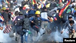 Coca growers, supporters of former President Evo Morales, run from tear gas as one of them kicks a tears gas canister during clashes with riot police in Sacaba, in the outskirts of Cochabamba, Bolivia, Nov. 15, 2019. 