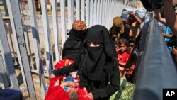 FILE - A Syrian woman caring a baby, walks with others to cross back to the border town of Tal Abyad in Syria from Turkey, at the border crossing in Akcakale, southeastern Turkey, June 17, 2015. 