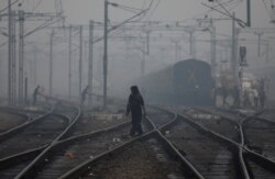 FILE - A woman crosses a railway line on a smoggy morning in New Delhi, India, Nov. 15, 2019.