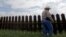 FILE -In this Sept. 16, 2015, photo, farmer Fausto Salinas stands along the border fence, in McAllen, Texas. The staggered fence or “wall,” costing $6.5 million per mile, runs along some 100 miles of Texas’ 1,254-mile border with Mexico. 