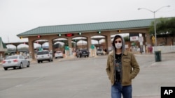 FILE- A pedestrian wears a protective mask as he passes the entrance to the McAllen Hidalgo International Bridge, March 21, 2020, in Hidalgo, Texas.