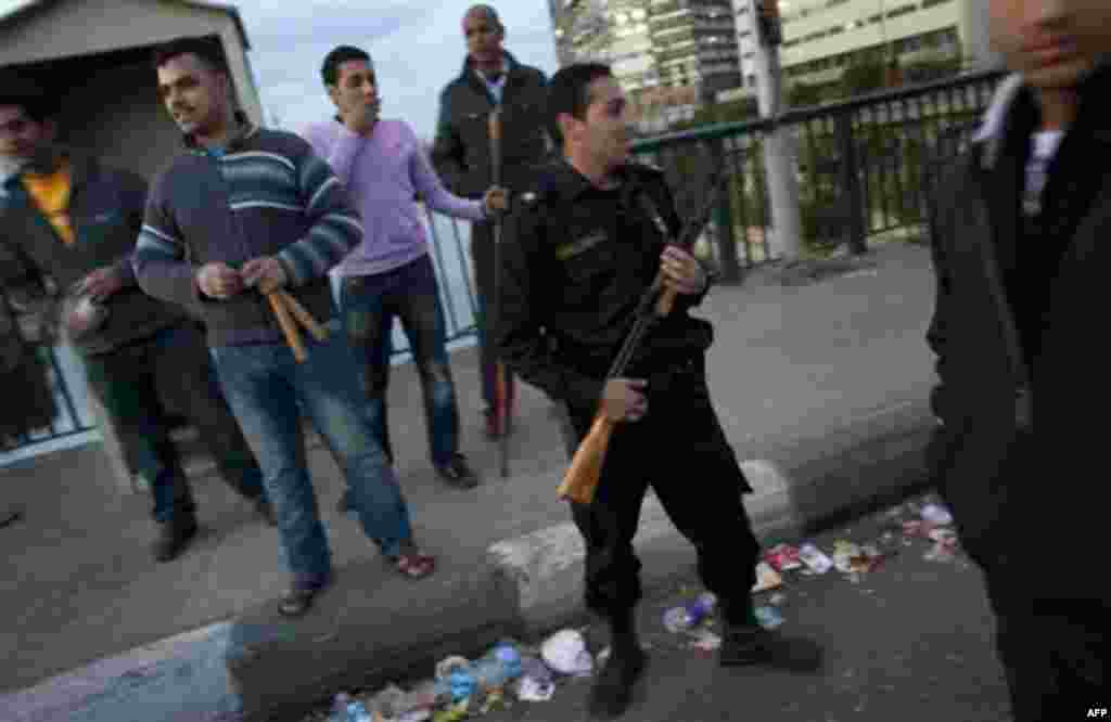 An Egyptian police officer stands guard next to one of the many neighborhood watch groups of men armed with metal bars and sticks at a checkpoint leading to a bridge in Cairo, Egypt, Monday, Jan. 31, 2011. A coalition of opposition groups called for a mi