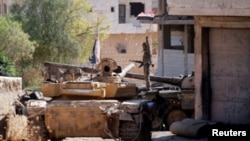 FILE - A Syrian army soldier holds a Syrian flag as he stands on a military vehicle in Khan Sheikhoun, Idlib, Syria, Aug. 24, 2019.