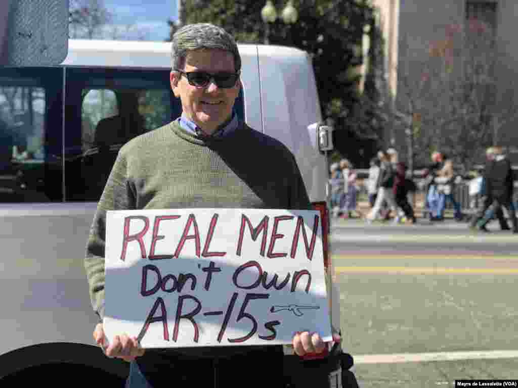 Manifestante exibe cartaz que diz "Homens de Verdade não andam armados com AR 15" 