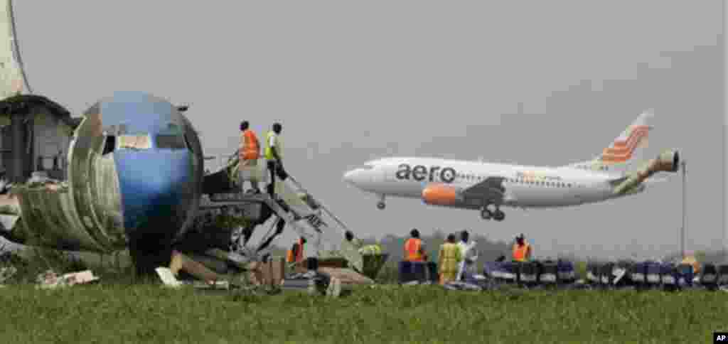 A passenger plane lands as workers dismantle an abandoned aircraft at Murtala Muhammed International Airport in Lagos, Nigeria.