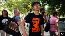 FILE - The leader of Pro-Democracy students Joshua Wong watches as police officers remove the barricades, Hong Kong, Oct. 14, 2014.