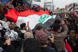 FILE - Anti government protesters carry a big Iraqi flag and chant anti-Iran and anti-U.S. slogans during the ongoing protests in Tahrir Square, Baghdad, Iraq, Jan. 10, 2020.