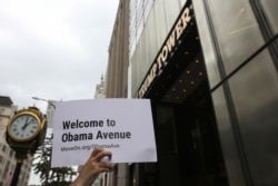 FILE - A demonstrator holds up a sign during a rally calling for the renaming of one block of Fifth Avenue "President Barack H. Obama Avenue," outside Trump Tower in New York City, Aug. 21, 2019.