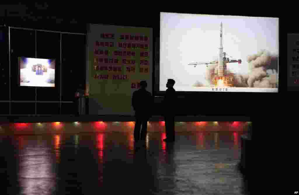 Oficiales de Corea del Norte permanecer cerca de una foto que representa el lanzamiento del sat&eacute;lite de cohetes en 2009 en la sala de exposiciones Tres Revoluciones de Pyongyang.