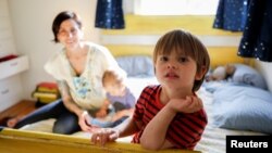 Three-year-old Wyatt Gries, right, sits on his bed inside his bedroom while his mother, Amanda Gries, holds his brother, Eli, in the Del Rey neighborhood of Los Angeles, California, April 4, 2017.