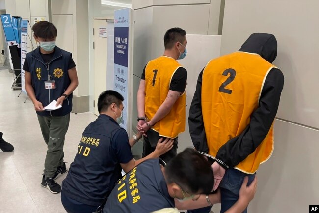 FILE - Police officers from the Taiwan Criminal Investigation Bureau search the bodies of two suspect who were deported from Bangkok and believed to be involved in scam cases in Cambodia as they arrive back at the Taoyuan International Airport in Taiwan, Aug. 18, 2022.