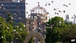 Burung merpati beterbangan di atas Taman Memorial Perdamaian di Hiroshima dengan Kubah Bom Atom pada latar belakang.