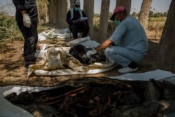 A doctor examines bodies that were found in a newly-discovered mass grave on the outskirts of Raqqa, Syria, Sept. 1, 2019. (Yan Boechat/VOA)