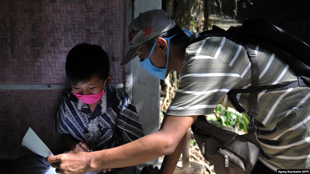 Guru SD Fransiscus Xaverius Fri Harna (kanan) mengajar di rumah siswanya di Magelang, Jawa Tengah, usai sekolah tutup akibat wabah virus Corona COVID-19. Beberapa guru mengambil medan berbahaya, cuaca buruk dan risiko tertular COVID-19, untuk menjangkau s