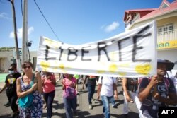 FILE - Demonstrators hold up banners and placards, one of which reads as 'freedom', during a national day of protest in Capesterre-Belle-Eau, on the French Caribbean archipelago of Guadeloupe, on Aug, 7, 2021.