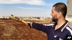 FILE - Free Syrian Army fighter, Bashar al Hajji, points towards the besieged Shi'ite village of Zahra in Aleppo, Oct. 17, 2012.