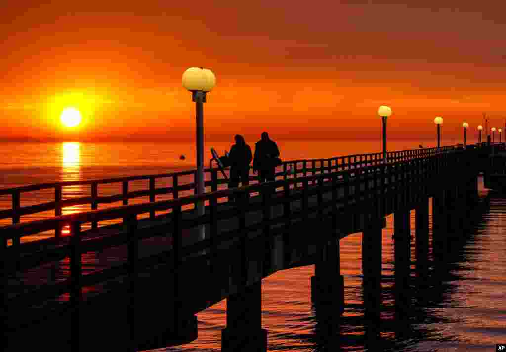 People walk on the pier at the Baltic Sea in Scharbeutz, Germany, as the sun rises.